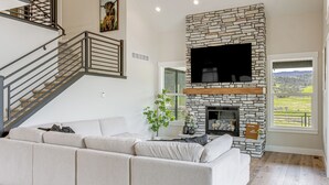 A modern living room with a stone fireplace, a large flat-screen TV, a sofa, and a staircase.