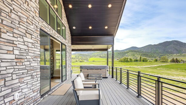 A covered outdoor deck with stone walls, a seating area, and a view of a green landscape and hills.
