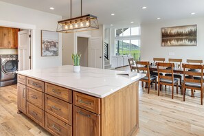 A modern kitchen with wooden cabinets, a marble island, and a dining area with wooden chairs and a table. - 5 Min From Lava Hot Springs, close to golf course & private Hot Tub (Lava Hot Springs)