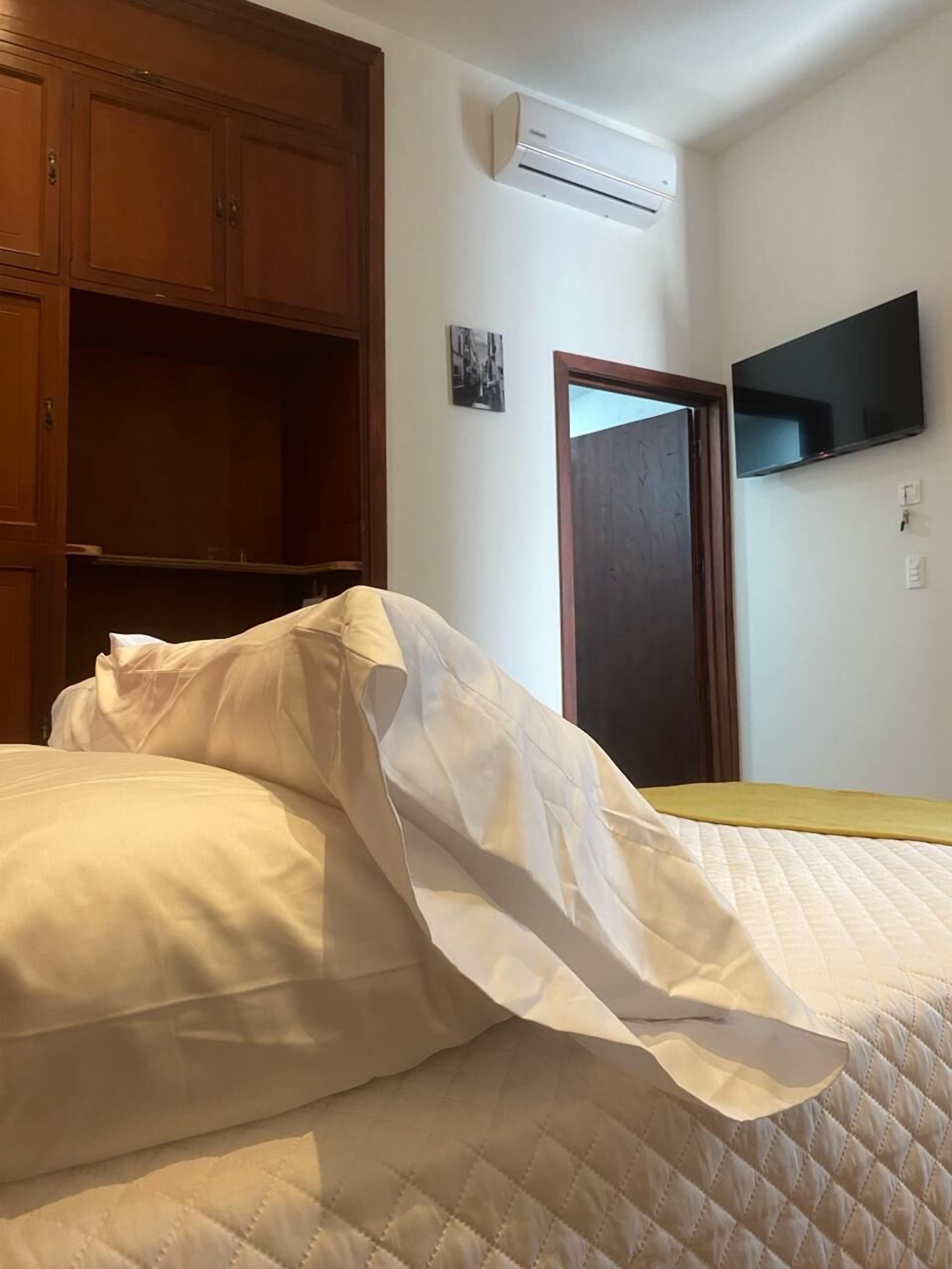 A bedroom with a bed, wooden wardrobe, air conditioning unit, and a television.