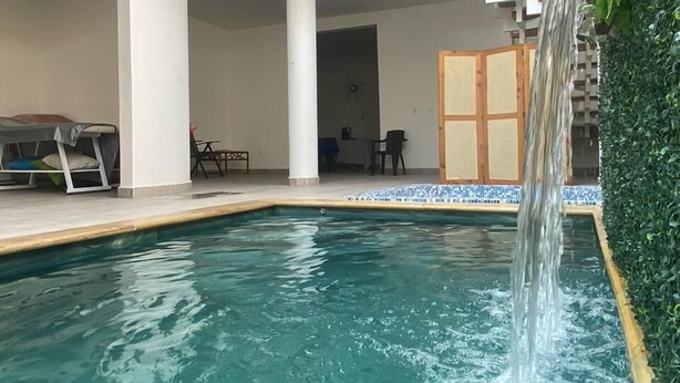 A swimming pool with a waterfall feature, a covered seating area, and a staircase leading to an upper level. - Hotel Boutique Iyarí (Palmira)