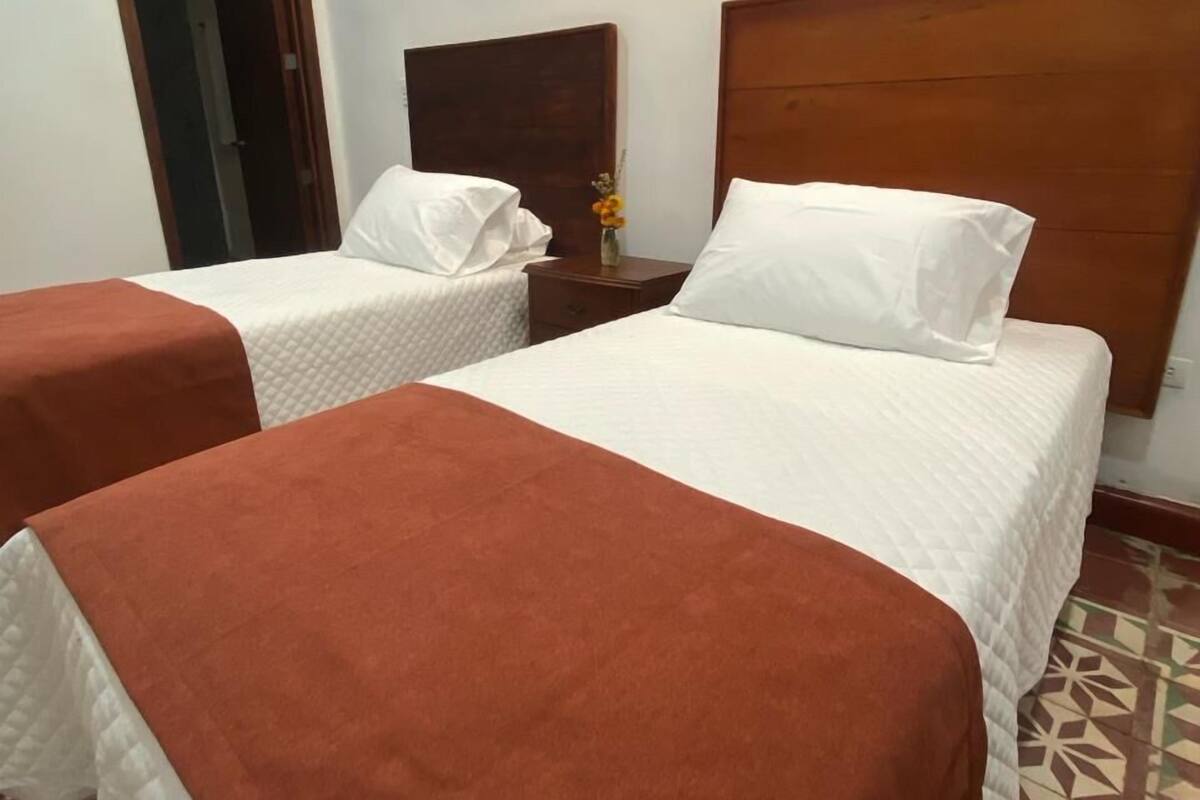 Une chambre d’hôtel avec deux lits, chacun doté d’une tête de lit en bois, d’une table de chevet ornée d’un vase de fleurs et d’un sol à motifs.