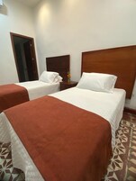 A hotel room with two beds, each with a wooden headboard, a nightstand with a vase of flowers, and a patterned floor.