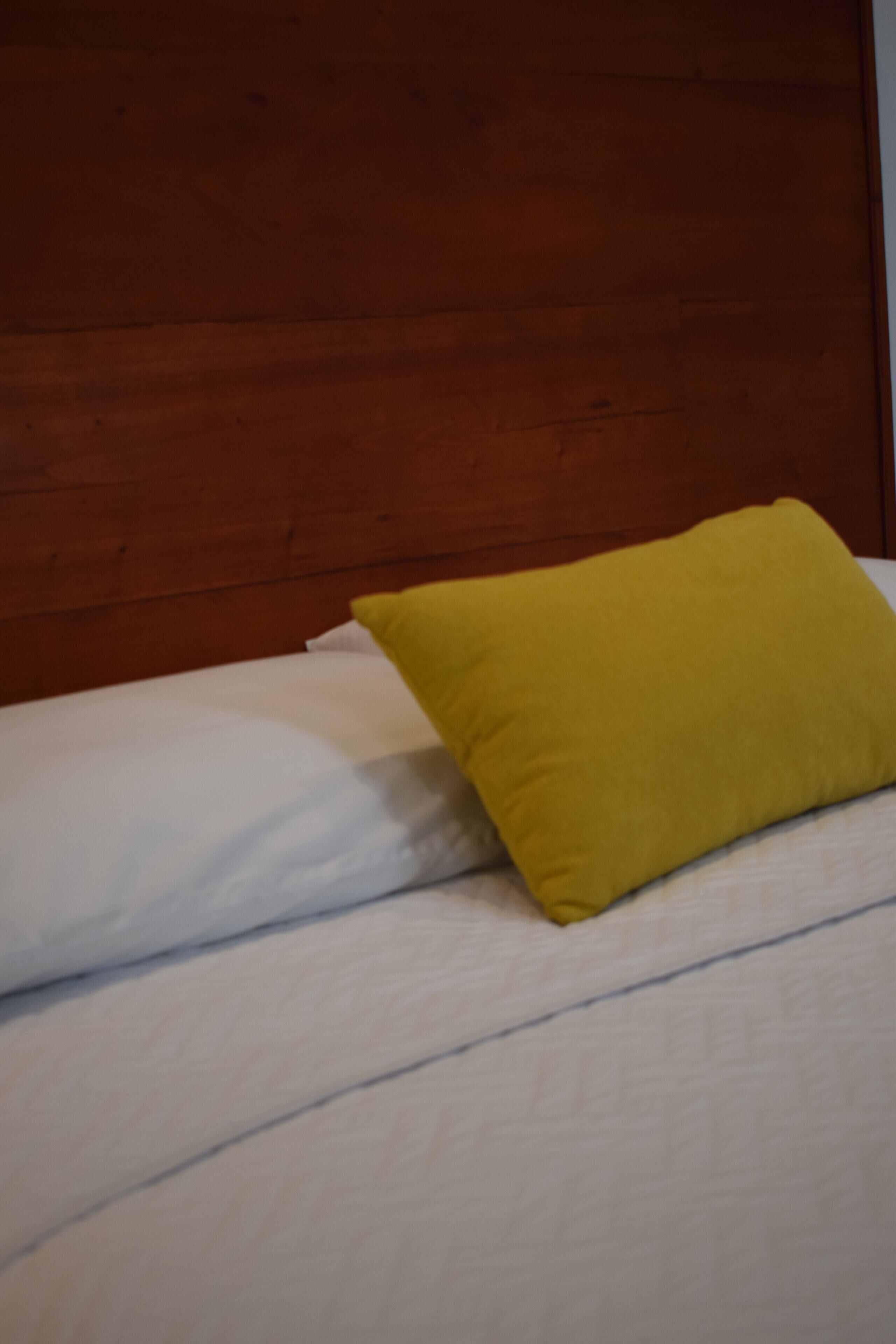 Una cama con ropa de cama blanca y una almohada amarilla.