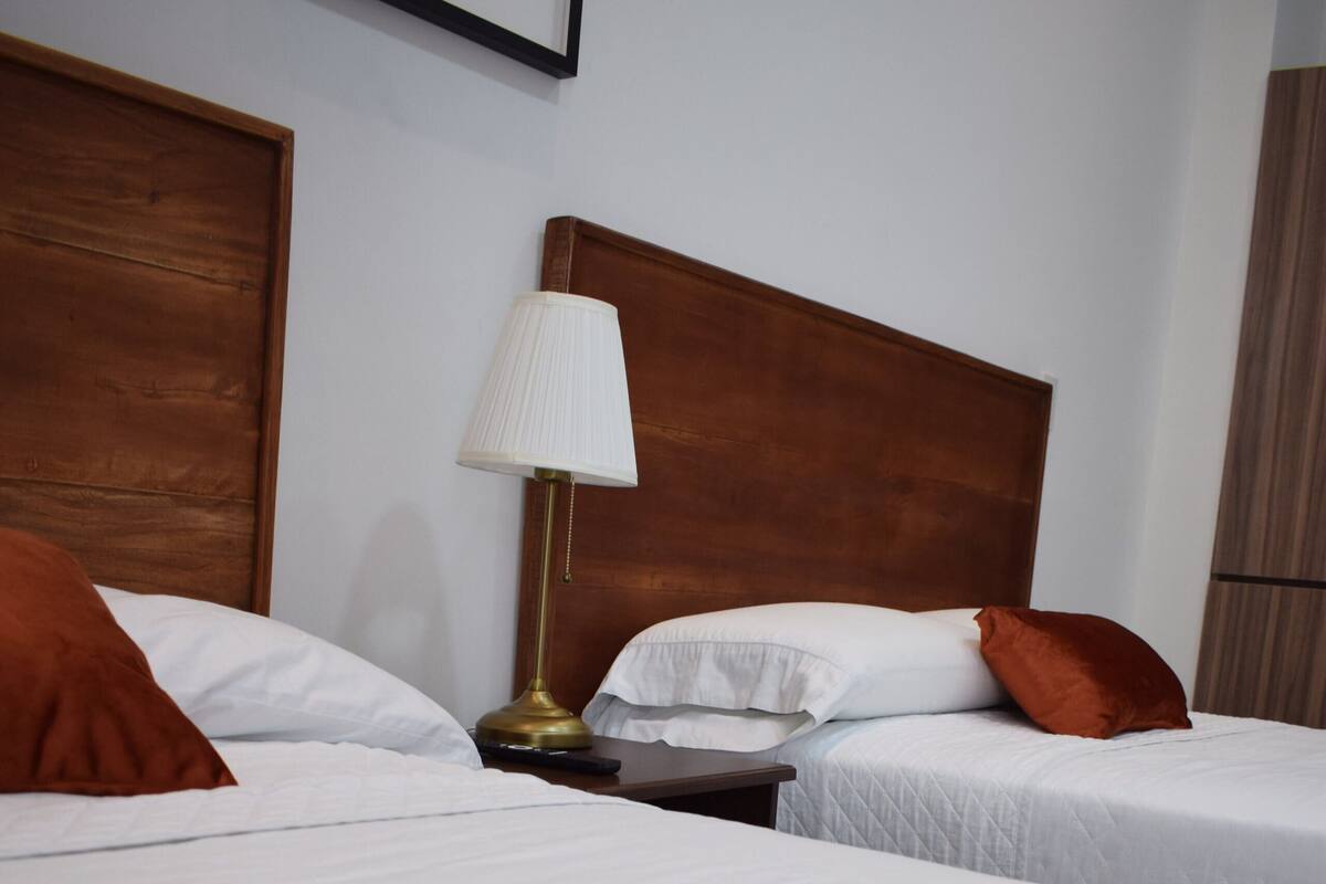 Une chambre d’hôtel avec deux lits, une table de chevet, une lampe et un tableau encadré au mur.
