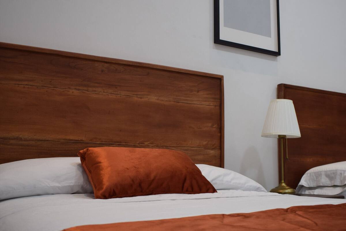 Un lit bien fait, avec une tête de lit en bois, un seul oreiller orange et une lampe de chevet.