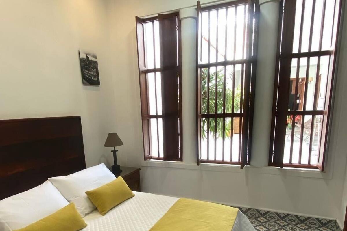 Une chambre d’hôtel avec un lit, une table de chevet, une lampe et une fenêtre donnant sur un paysage verdoyant.