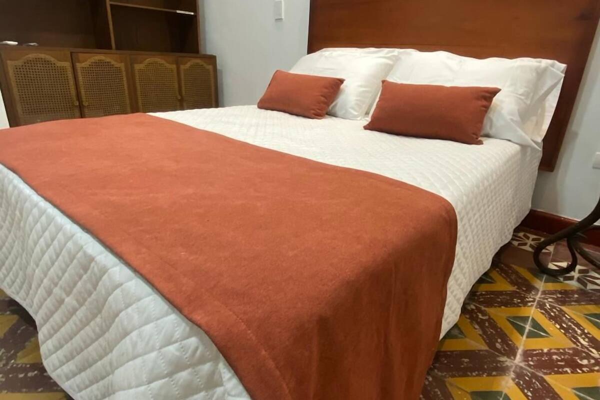 Un lit avec une couverture marron, des oreillers blancs et une tête de lit en bois.