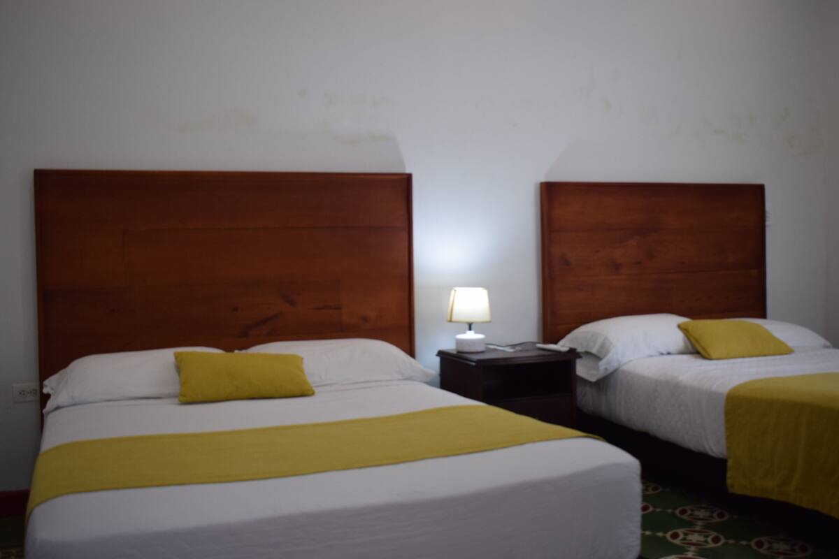 Deux lits simples avec des têtes de lit en bois, du linge de lit blanc et des touches de couleur jaune.