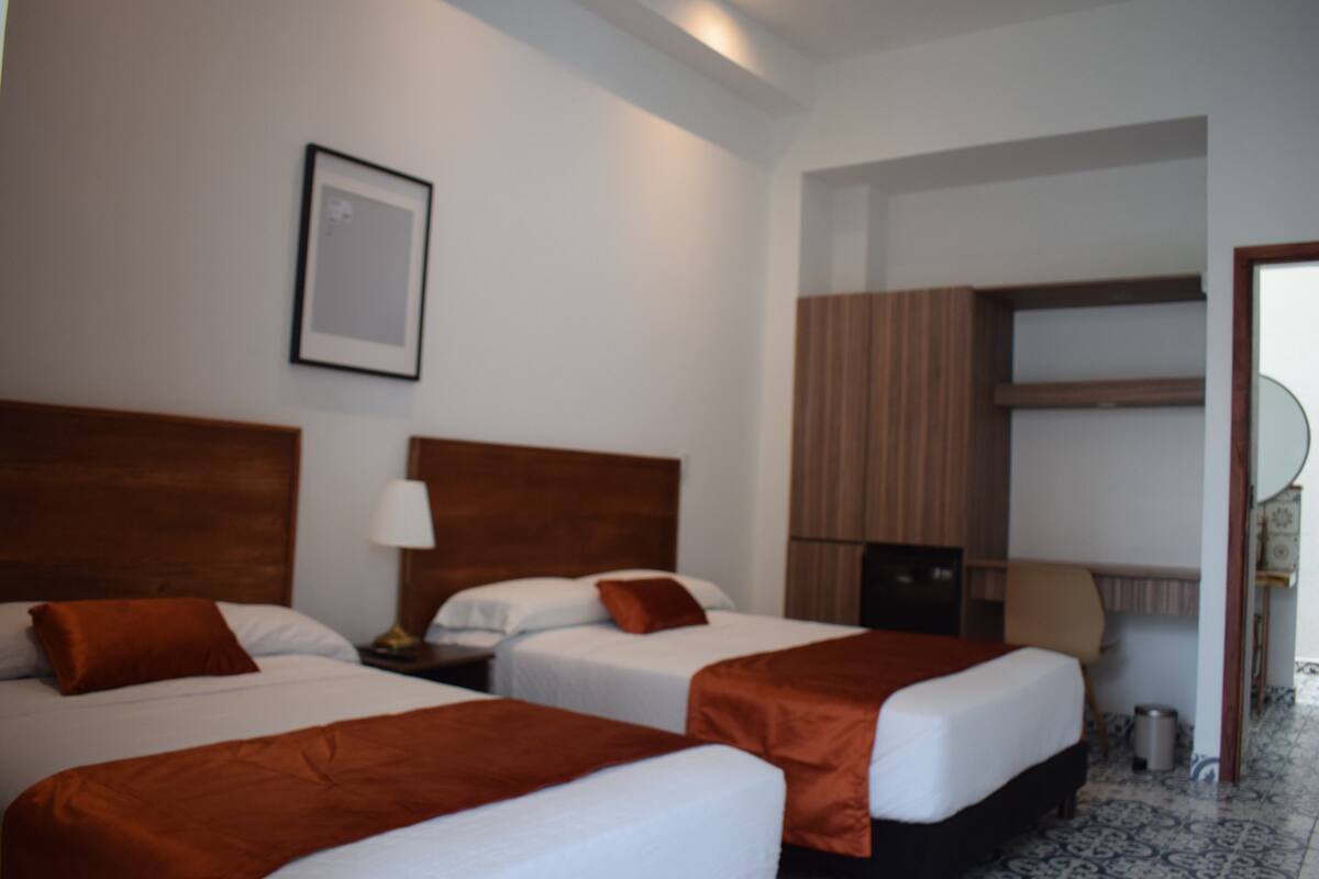 Une chambre d’hôtel avec deux lits, un bureau et une chaise.