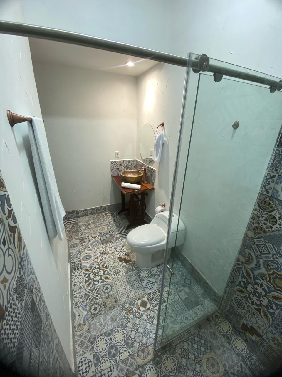 Een badkamer met een vloer met patroon, een toilet, een wastafel met spiegel en een handdoekhouder.