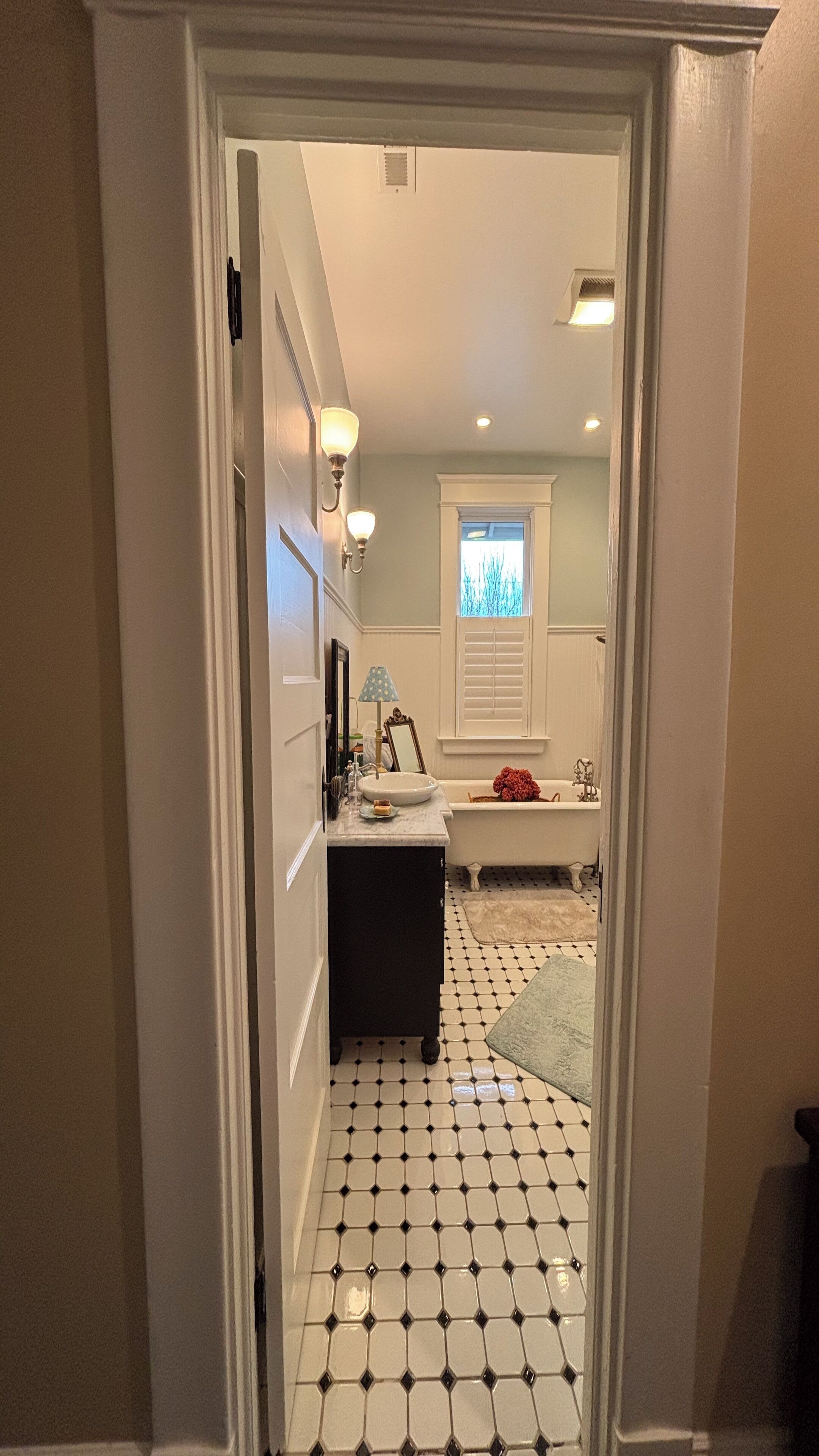 Un pasillo que conduce a un baño con un lavamanos blanco, un espejo y una bañera.