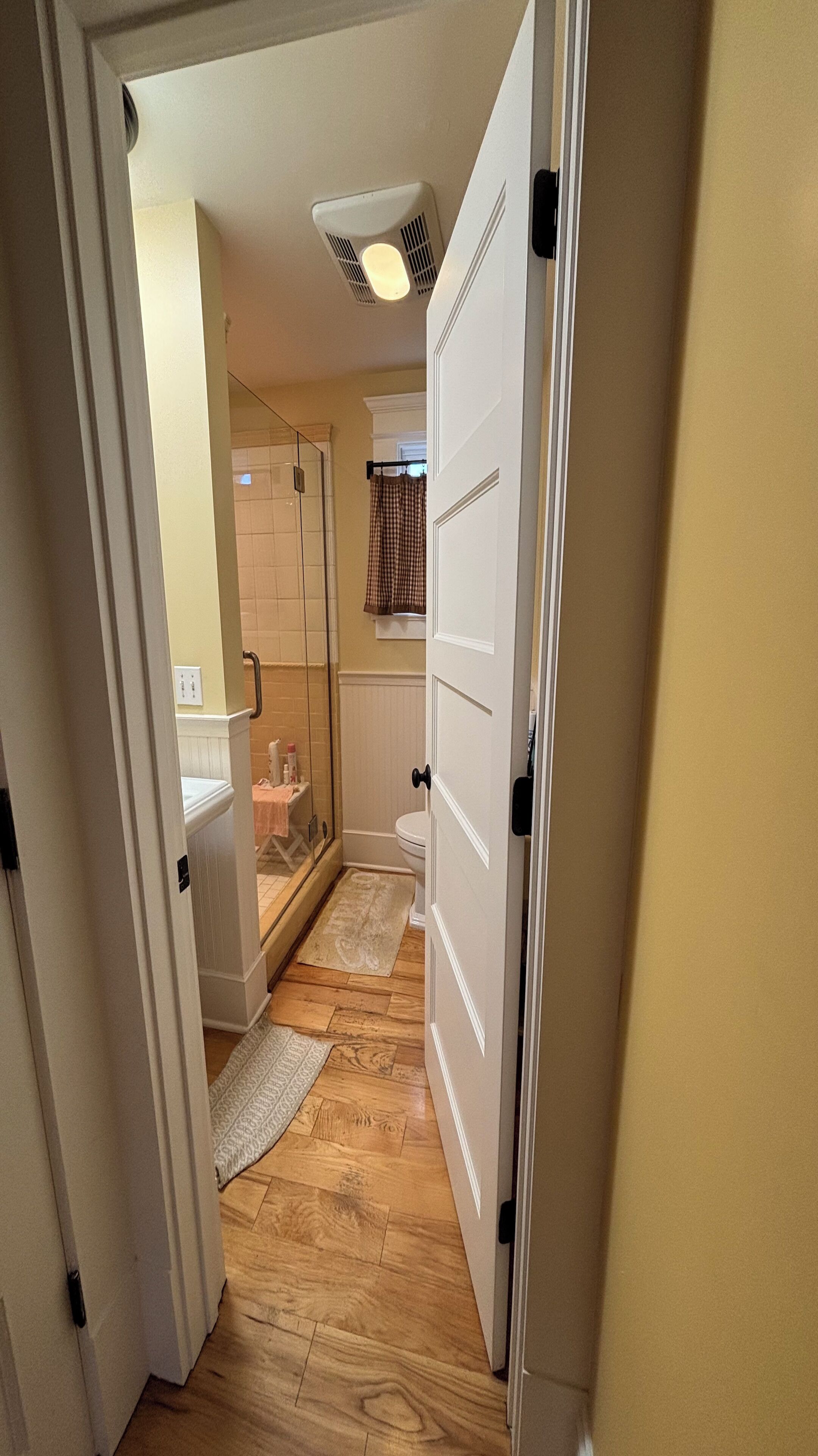 Un pasillo estrecho que conduce a un baño con ducha, inodoro y un perchero para toallas.