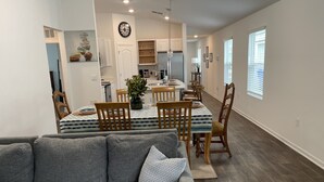 A modern living room with a gray sofa and a dining area with wooden chairs and a patterned tablecloth. - Breeze Retreat (St. Augustine)