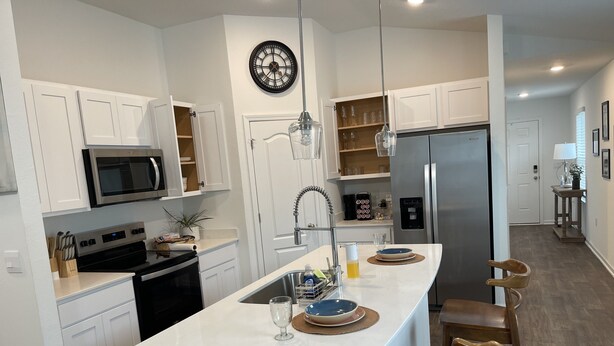 A modern kitchen with white cabinetry, a central island with bar stools, stainless steel appliances, and a clock on the wall. - Breeze Retreat (St. Augustine)
