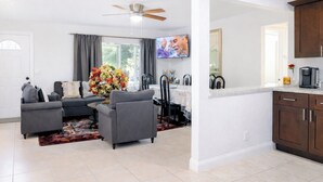 A modern living room with grey sofas, a dining area with a table and chairs, a kitchen with dark cabinets, and a ceiling fan. - Family-Friendly Home Near the Beach Pets Welcome (West Palm Beach)