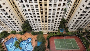 A high-rise building with multiple balconies, a swimming pool, and a tennis court.