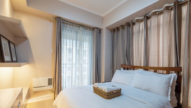 A hotel room with a bed, a bedside table, a wall-mounted air conditioner, and a window with curtains.