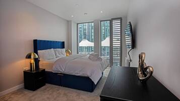 A modern bedroom with a bed, bedside tables, a desk, and a large window with a city view.