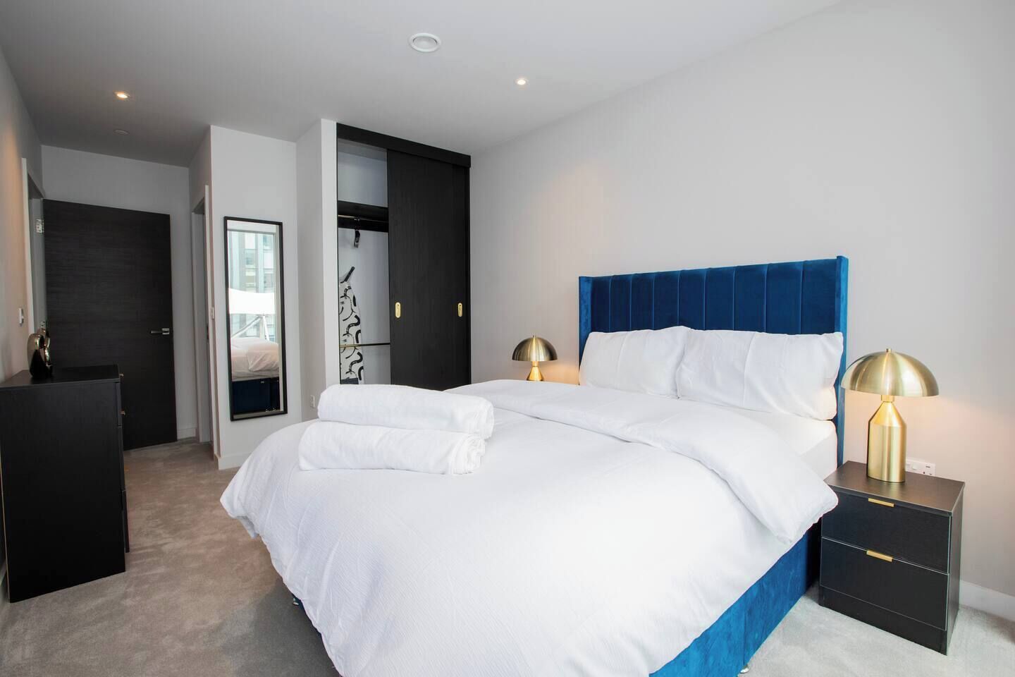 Una habitación de hotel moderna con una cama grande, un armario, un escritorio y una mesita de noche con lámparas.