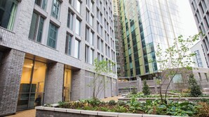 Een modern gebouw met een bakstenen gevel, grote ramen en een aangelegde binnentuin met planten en een pad.