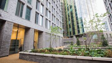 A modern building with a brick facade, large windows, and a landscaped courtyard with plants and a pathway.