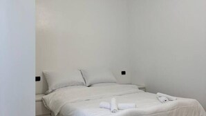 Un letto singolo con biancheria bianca e un asciugamano arrotolato sopra.