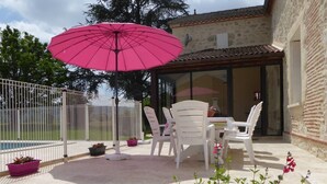 Eine Terrasse mit Tisch, Stühlen, einem pinken Sonnenschirm und Topfpflanzen.