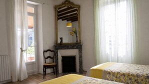 Ein Zimmer mit Kamin, zwei Betten mit Blumenoptik, einem Sessel und einem großen Spiegel.