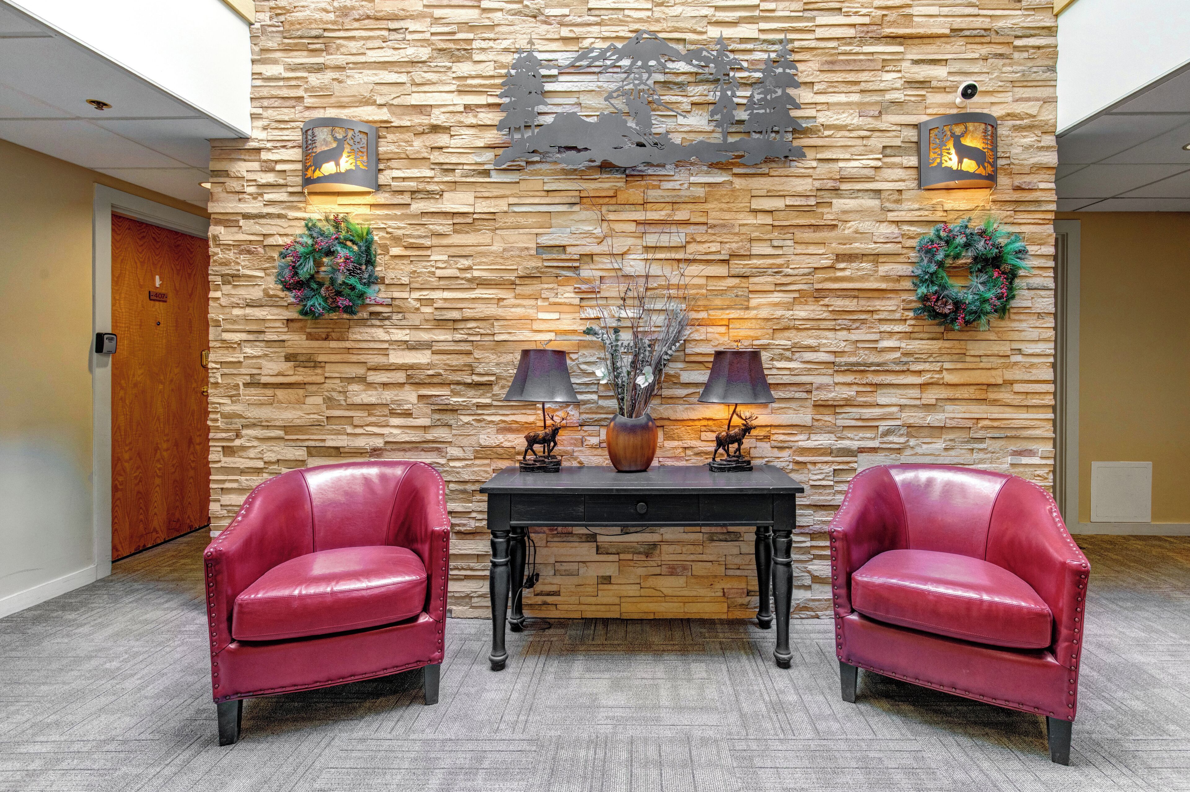A lobby with a stone wall, two red leather chairs, a black table with decorative items, and two wall-mounted light fixtures.