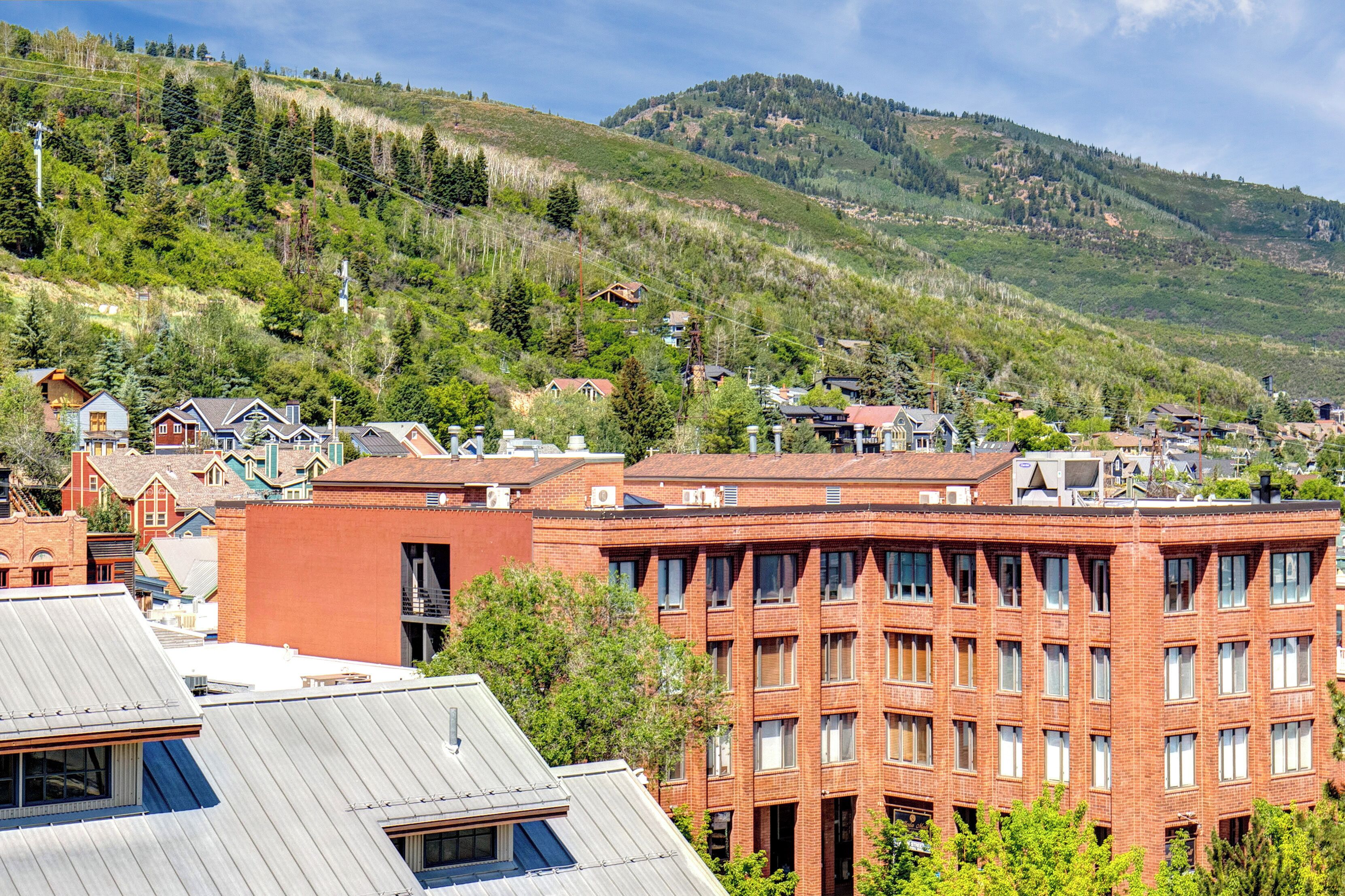 A town with a prominent red brick building, surrounded by greenery and hills.