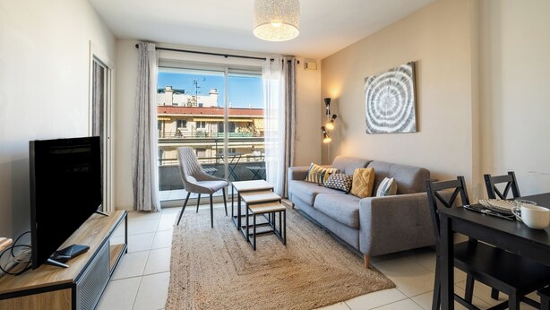 A modern living room with a TV, sofa, dining table, and chairs. - Appartement Olivier - Welkeys (Antibes)