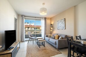 A modern living room with a TV, sofa, dining table, and chairs. - Appartement Olivier - Welkeys (Antibes)