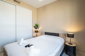Habitació d'hotel amb un llit, làmpades de nit, una planta i un penjador de tovalloles.