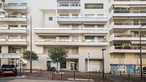 A multi-story residential building with balconies, a small shop on the ground floor, and a parked car. - Appartement Olivier - Welkeys (Antibes)