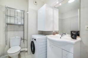 A modern bathroom with a toilet, washing machine, and sink. - Appartement Olivier - Welkeys (Antibes)