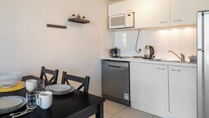 A modern kitchen with white cabinets, a microwave, and a dishwasher. There is a dining table with plates, cups, and cutlery. - Appartement Olivier - Welkeys (Antibes)