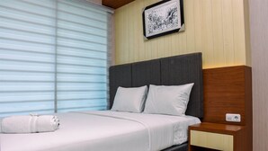 Uma cama bem arrumada com lençóis brancos, cabeceira cinza e mesa de cabeceira de madeira com gaveta.