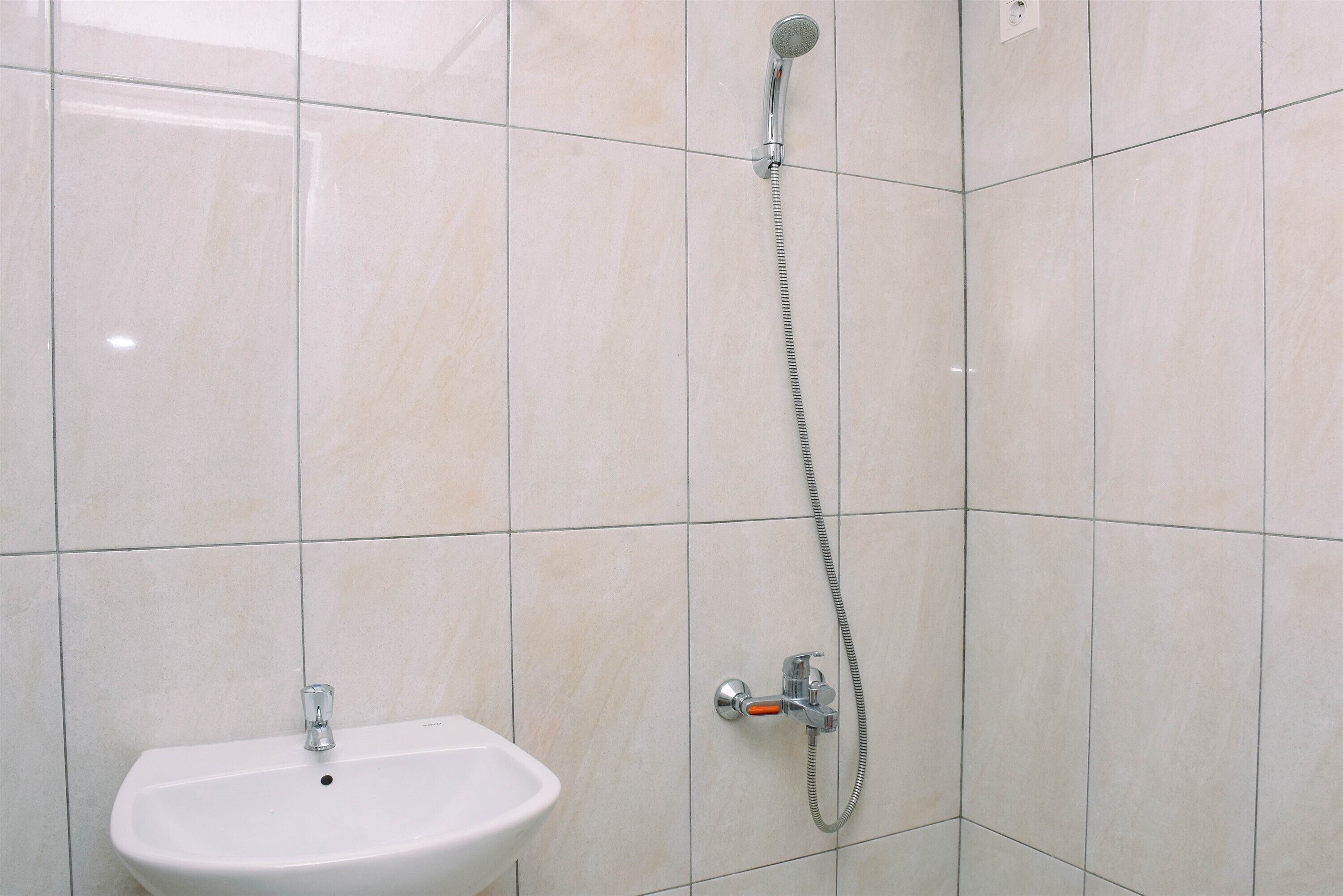 Un baño con lavamanos blanco, cabezal de ducha de mano y grifo empotrado en la pared.