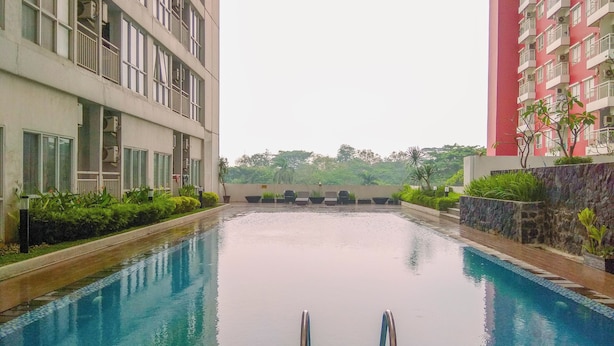 A swimming pool with a clear view of the surrounding buildings, a stone wall, and some greenery. - Cozy Stay Studio Room At Taman Melati Margonda Apartment (Depok)