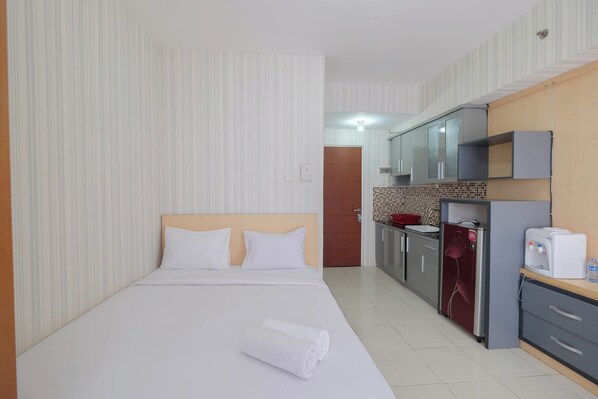 A hotel room with a bed, a small kitchenette, and a bathroom visible through an open door. - Cozy Stay Studio Room At Taman Melati Margonda Apartment (Depok)