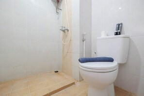 A bathroom with a toilet, a shower, and a toilet paper holder. - Cozy Stay Studio Room At Taman Melati Margonda Apartment (Depok)