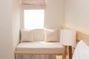 A small, neatly arranged bedroom with a single bed, a bedside lamp, and a window with a light-colored curtain. - Fully Furnished And Tidy Studio At Grand Kamala Lagoon Apartment (Bekasi)