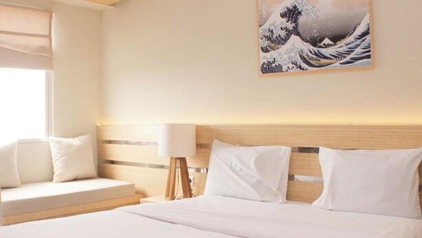 Hotelkamer met een bed, nachtkastje met lamp, wanddecoratie en raam met zonwering.