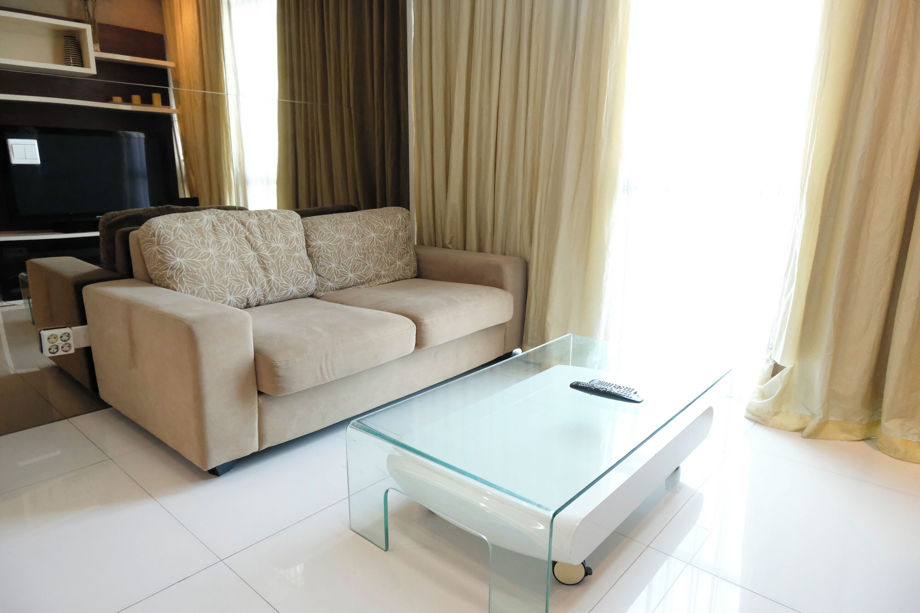 Una sala de estar con una mesa de centro de vidrio, sofá color beige y un televisor de pantalla plana.