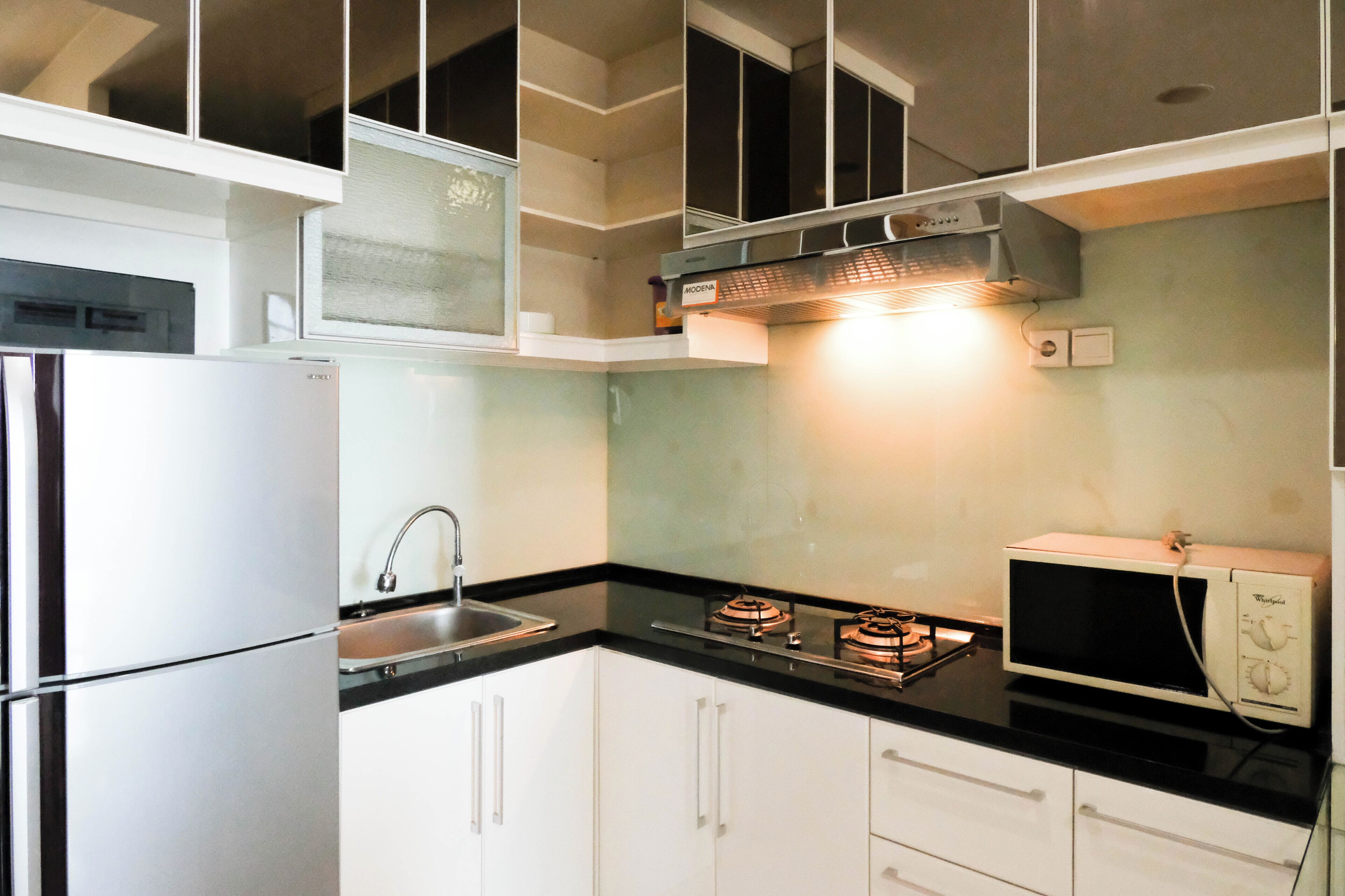 A compact kitchen with white cabinets, a stainless steel refrigerator, a sink, a gas stove, and a microwave.