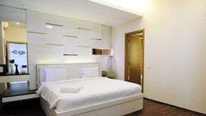 A modern bedroom with a large bed, a bedside table, a mirror, and a wooden door. - Spacey 2Br With Access Mall At Apartment Aryaduta Residence Surabaya (Surabaya)