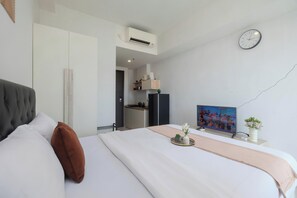Ein modernes Hotelzimmer mit einem großen Bett, einem Flachbildfernseher, einer Uhr und einer Küchenzeile im Hintergrund.