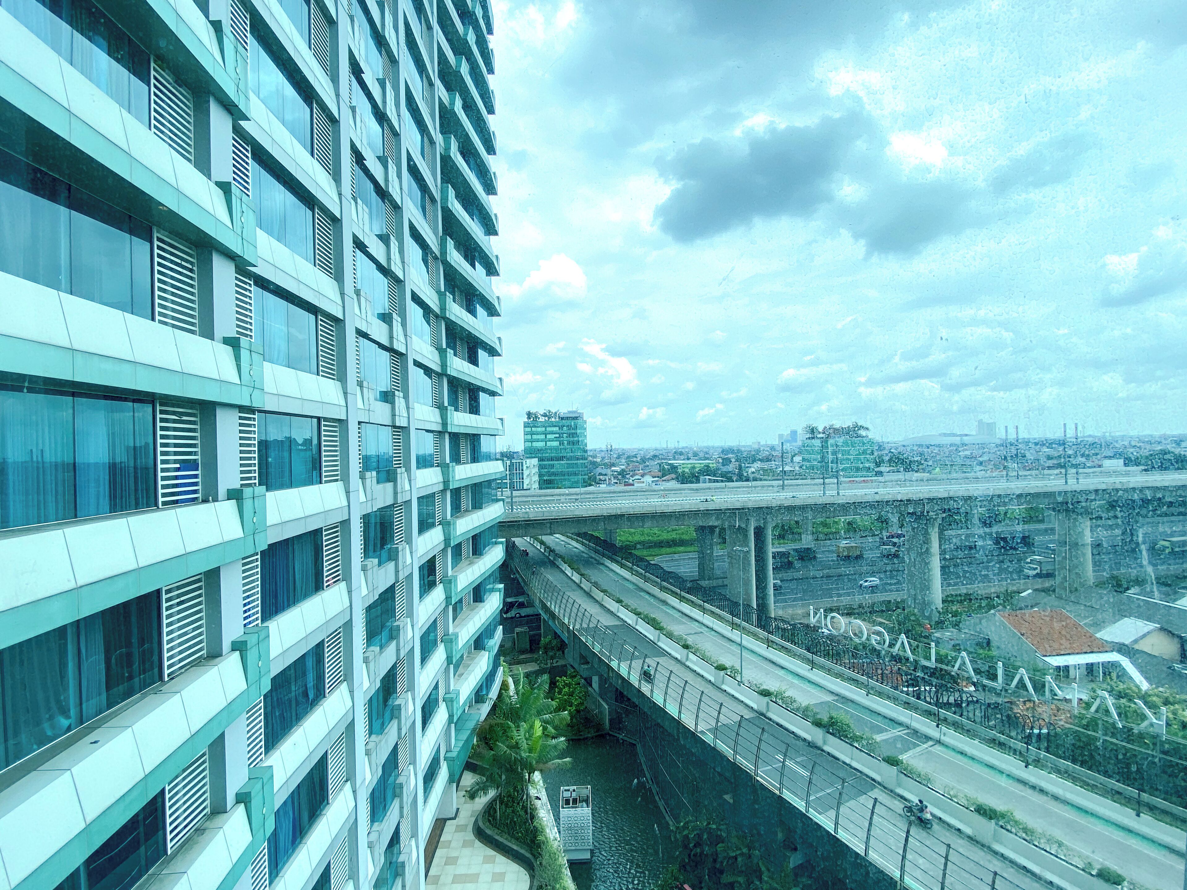 A modern high-rise building with multiple floors, a pedestrian bridge, and a cityscape in the background.