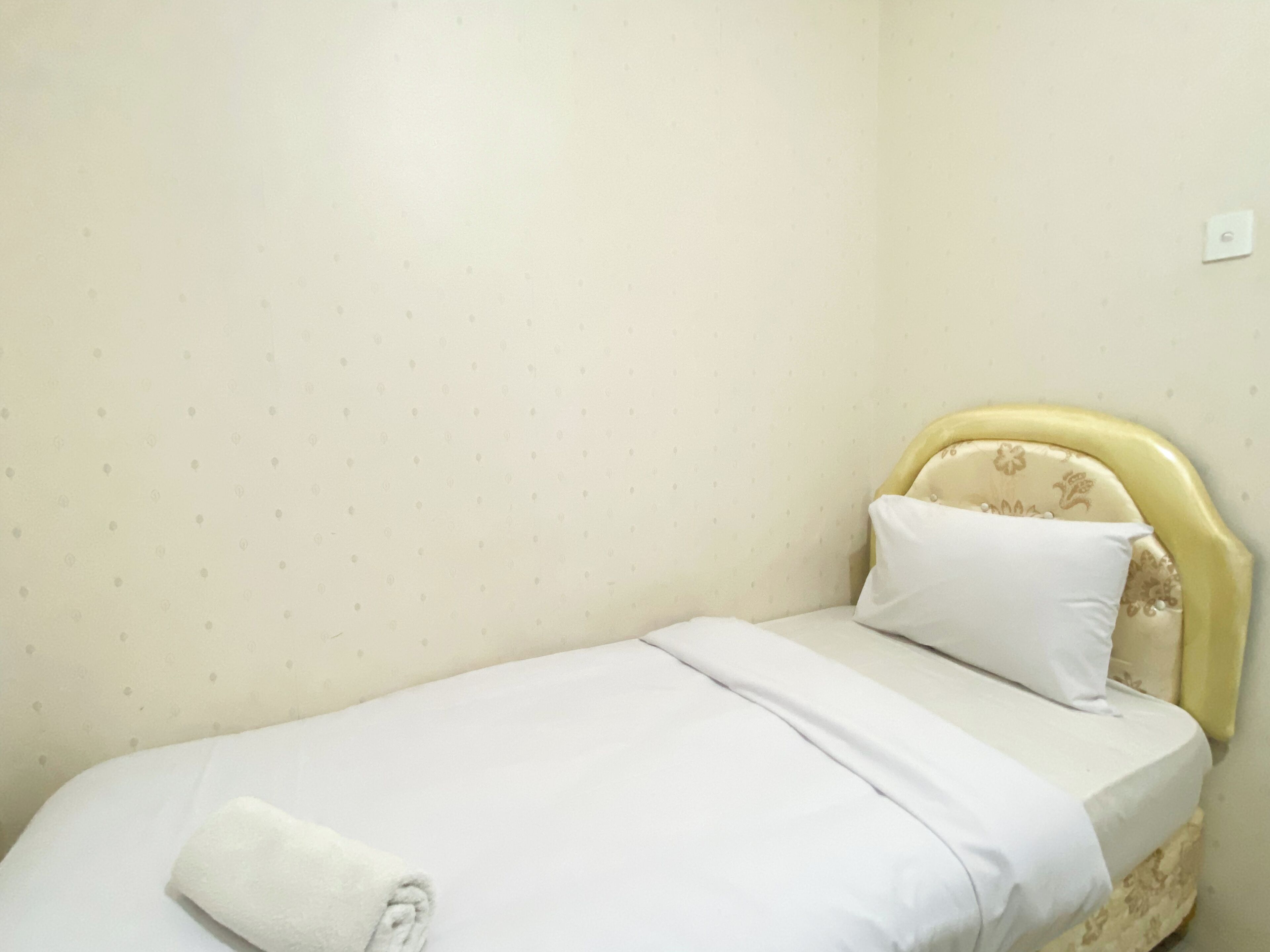 A small, single-bed room with a yellow headboard, white bedding, and a patterned wall.